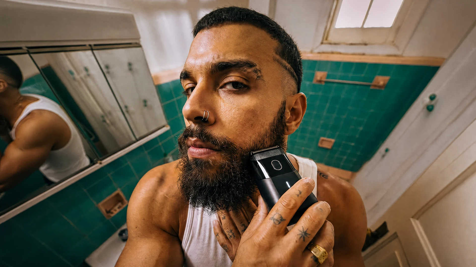 Homem barbudo usando o barbeador em um banheiro com azulejos verdes